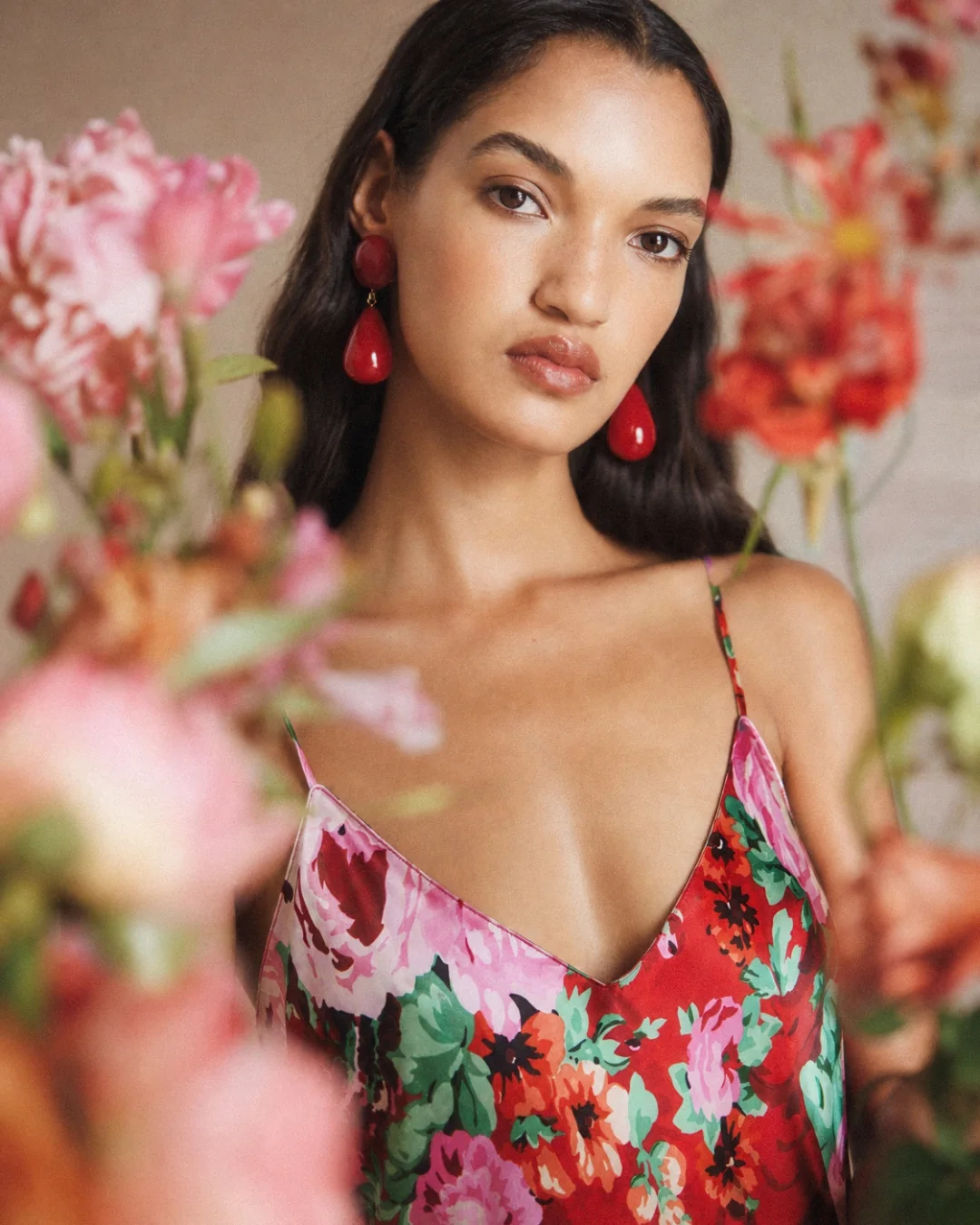 AI fashion campaign visual: model in a red floral silk dress beside a mirror and flowers